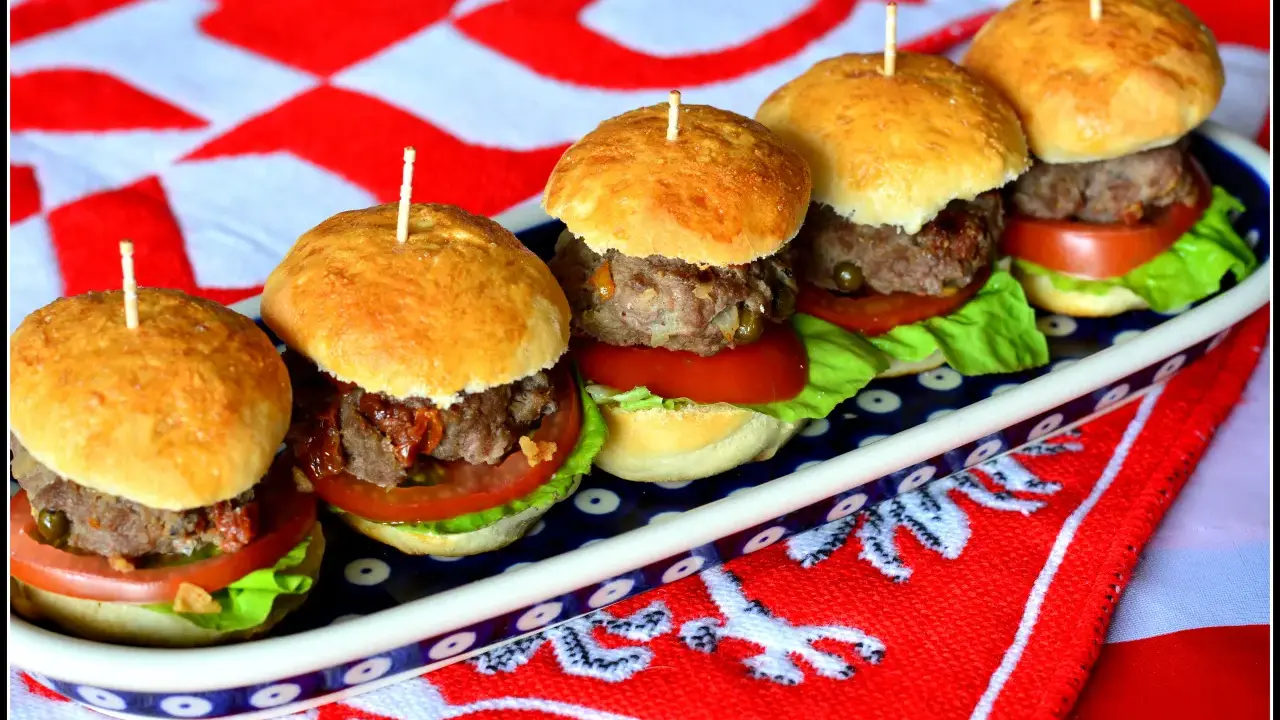 Rząd pięciu mini burgerów z mięsem, sałatą i pomidorem na talerzu.