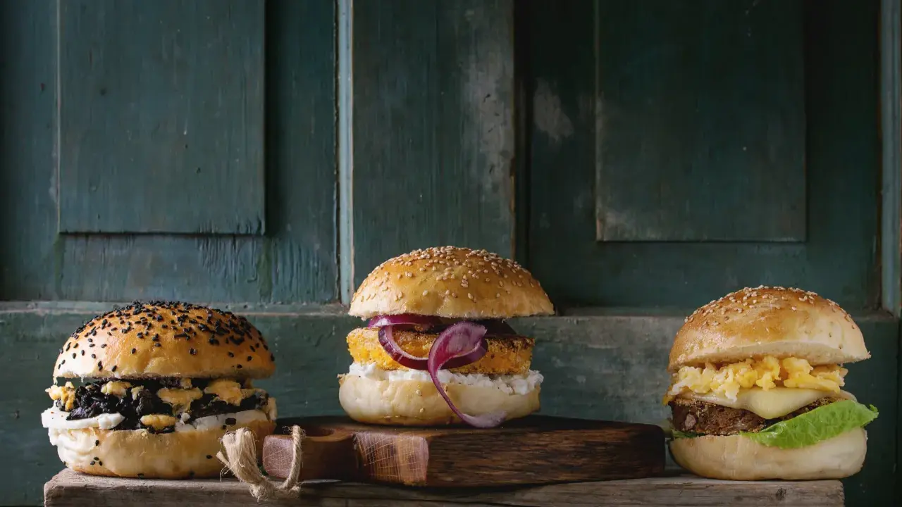 Trzy apetyczne burgery na drewnianej desce. Zastanawiasz się, ile kosztuje burger?
