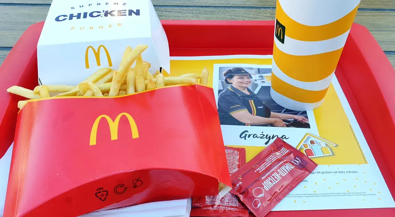 Duże frytki McDonald's w czerwonym opakowaniu, obok pudełka z burgerem i kubka z napojem.