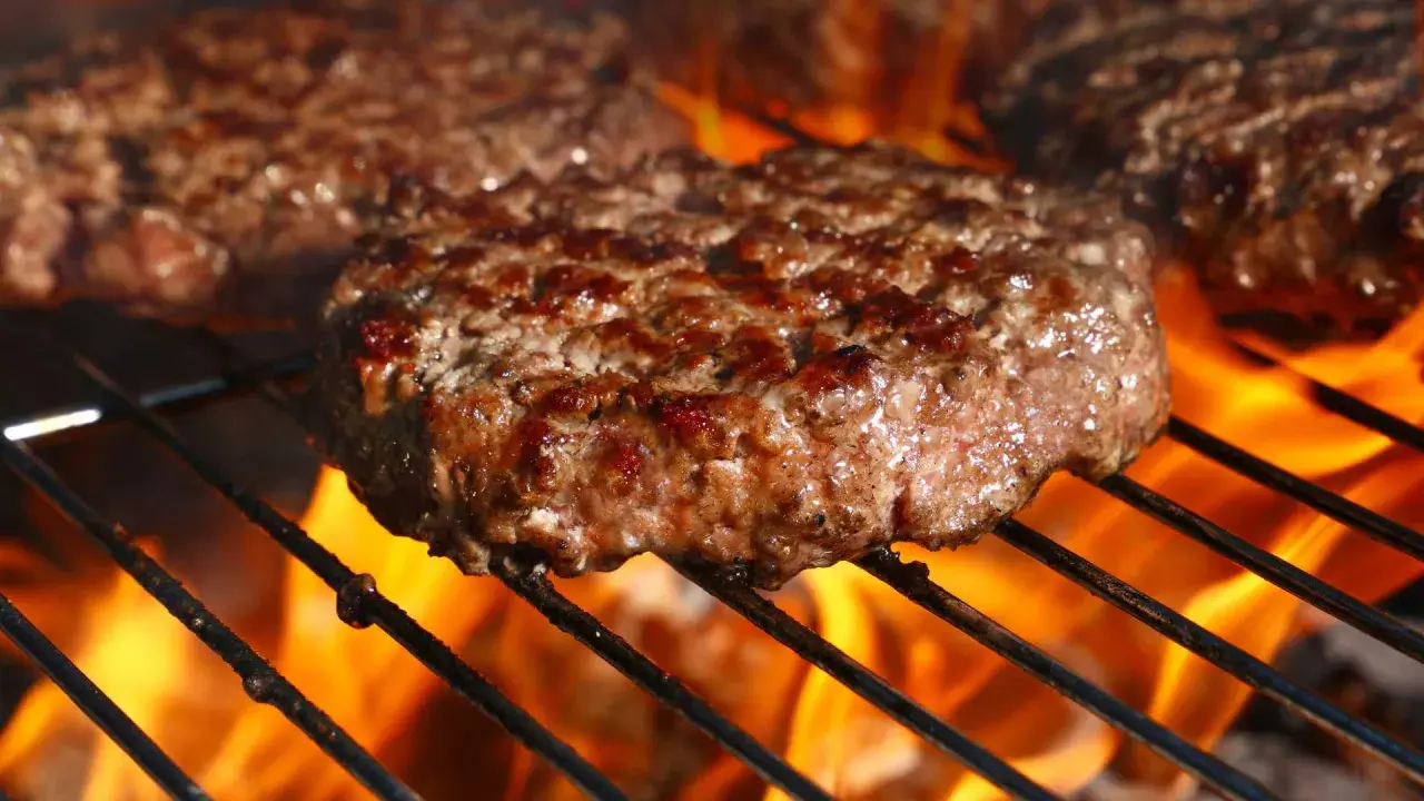 Soczyste burgery wołowe smażące się na grillu z płomieniami.