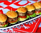 Rząd pięciu mini burgerów z mięsem, sałatą i pomidorem na talerzu.