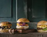 Trzy apetyczne burgery na drewnianej desce. Zastanawiasz się, ile kosztuje burger?