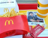 Duże frytki McDonald's w czerwonym opakowaniu, obok pudełka z burgerem i kubka z napojem.