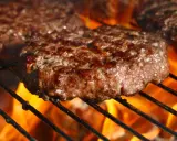 Soczyste burgery wołowe smażące się na grillu z płomieniami.