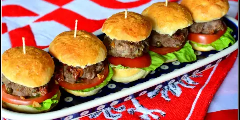 Rząd pięciu mini burgerów z mięsem, sałatą i pomidorem na talerzu.