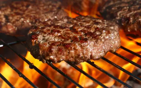 Soczyste burgery wołowe smażące się na grillu z płomieniami.