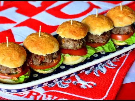 Rząd pięciu mini burgerów z mięsem, sałatą i pomidorem na talerzu.