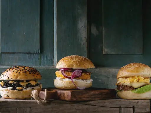 Trzy apetyczne burgery na drewnianej desce. Zastanawiasz się, ile kosztuje burger?