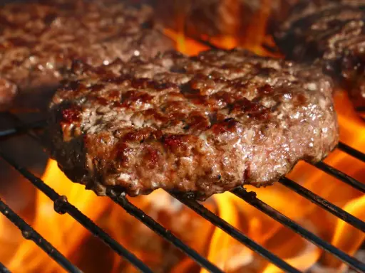 Soczyste burgery wołowe smażące się na grillu z płomieniami.