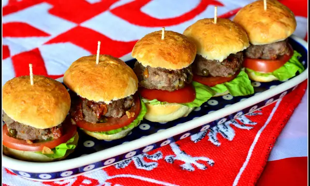 Rząd pięciu mini burgerów z mięsem, sałatą i pomidorem na talerzu.