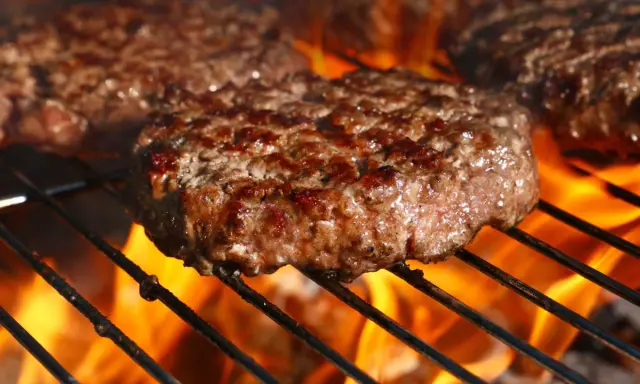 Soczyste burgery wołowe smażące się na grillu z płomieniami.