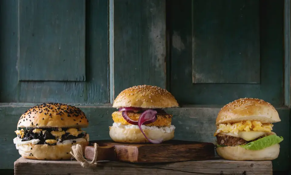 Trzy apetyczne burgery na drewnianej desce. Zastanawiasz się, ile kosztuje burger?