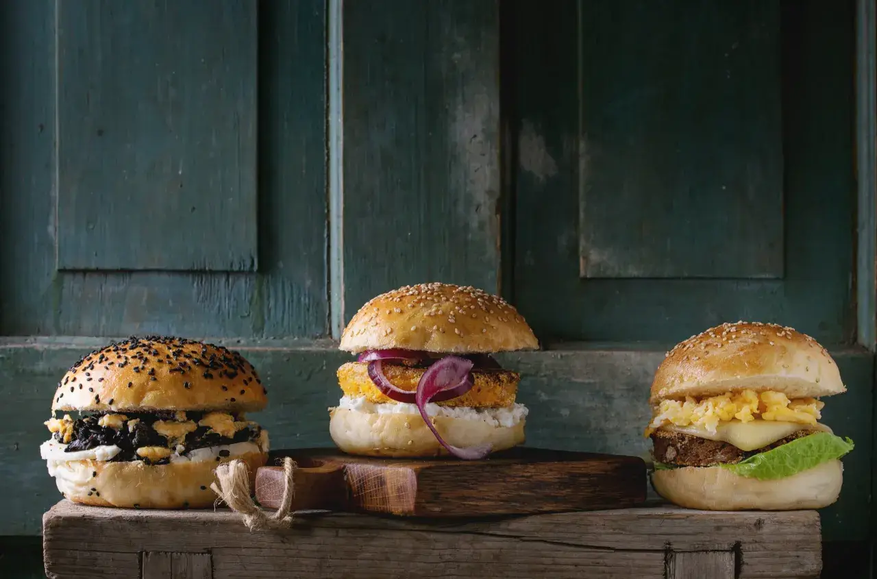 Trzy apetyczne burgery na drewnianej desce. Zastanawiasz się, ile kosztuje burger?
