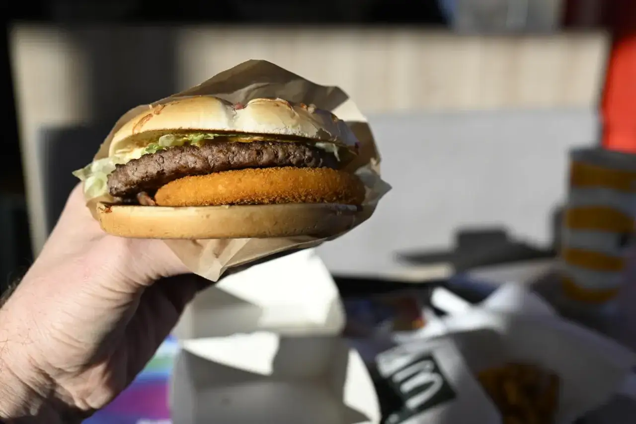 Ręka trzyma soczystego burgera drwala z chrupiącą cebulką. Idealny na szybki posiłek.