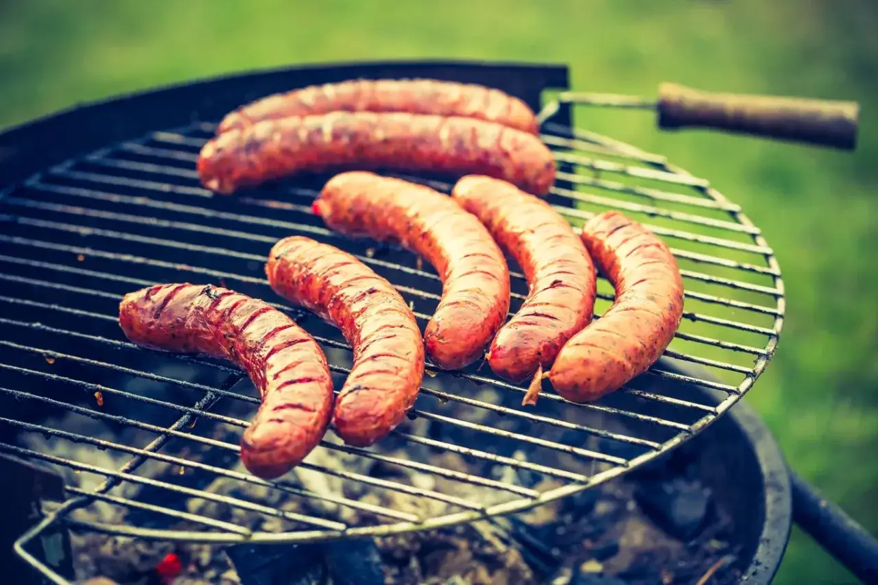 człowiek nacinający kiełbasę przed grillowaniem
